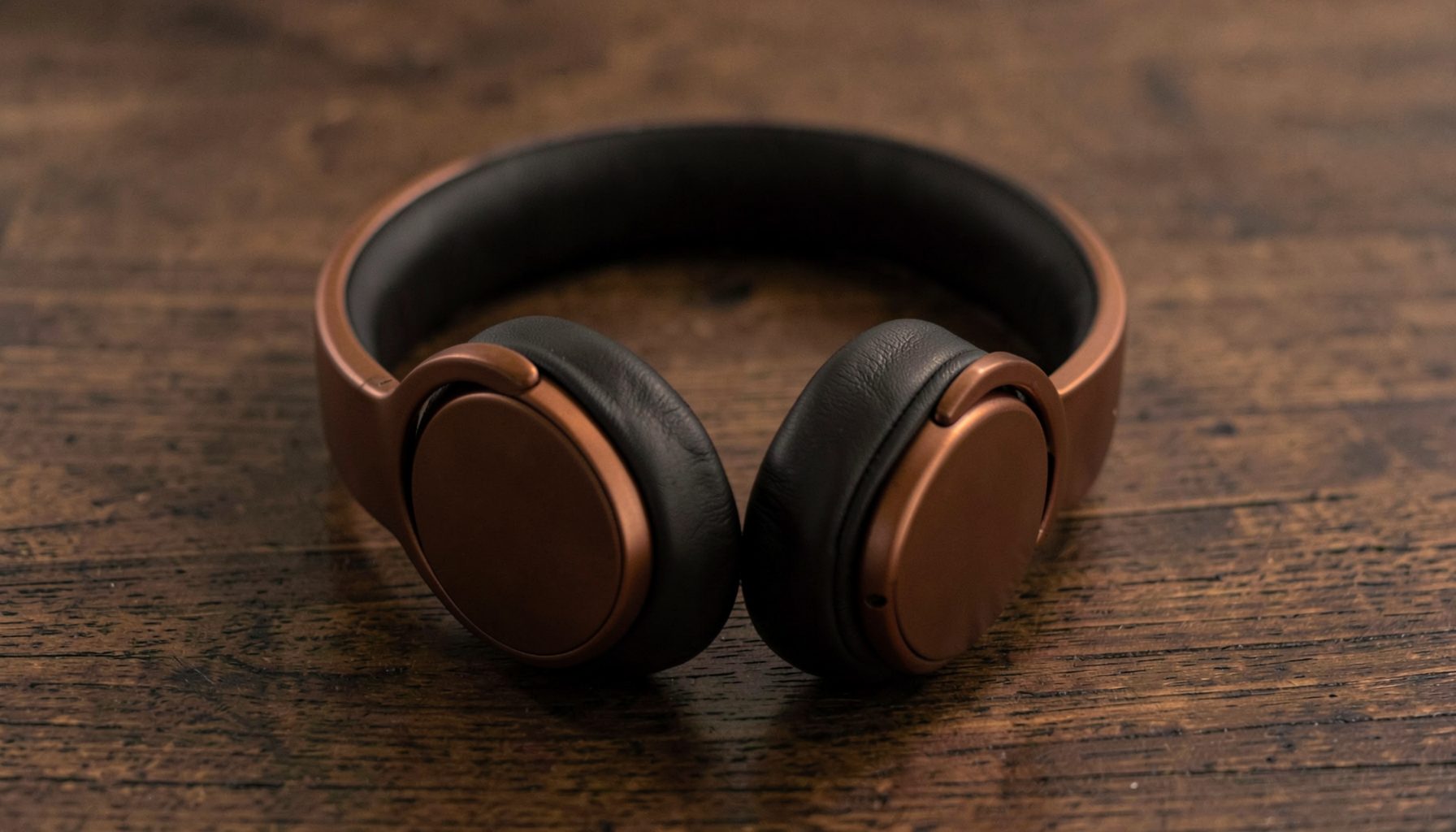 A pair of headphones resting on a wooden surface, deep browns and muted copper tones, calm and intimate.