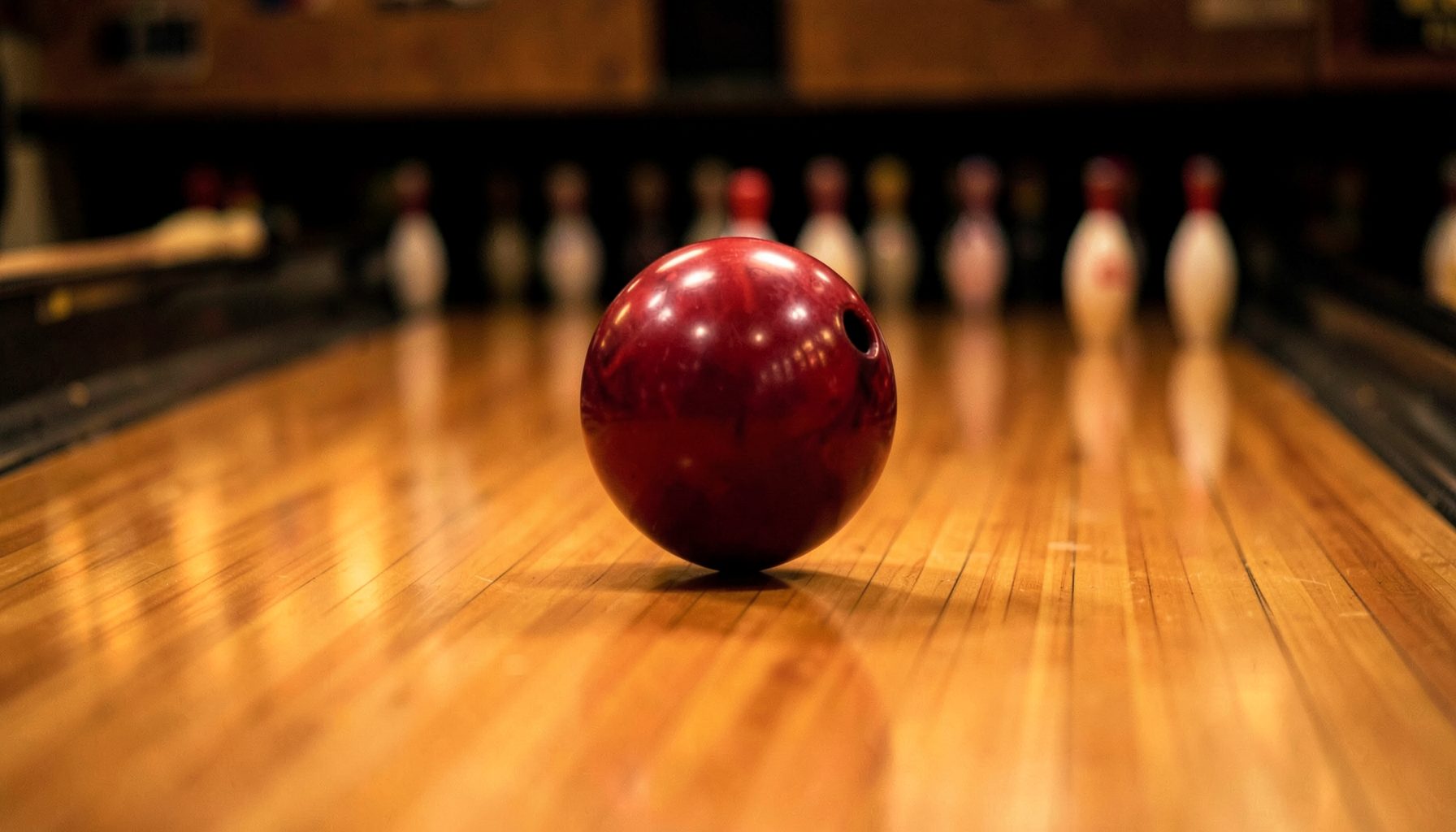 A shiny bowling ball rolling down a polished wooden lane toward pins, warm amber lighting, dynamic motion blur