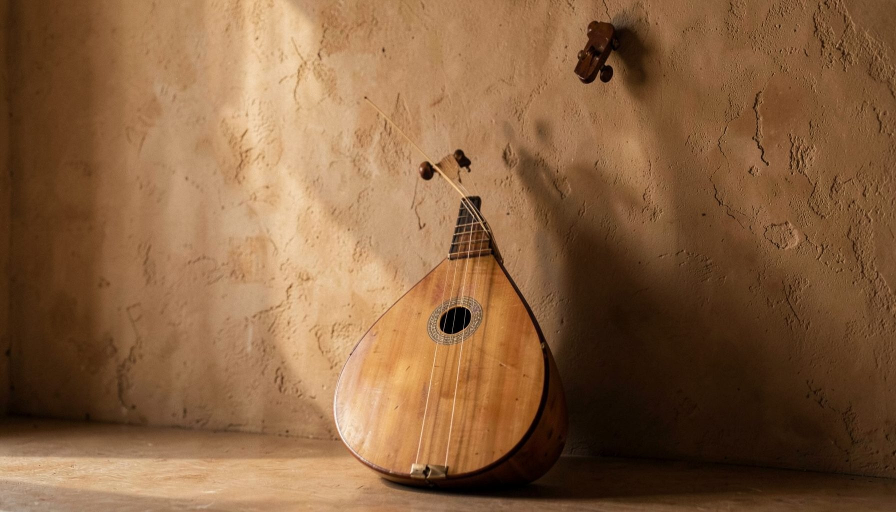 An oud instrument leaning against a textured wall, warm earth tones and soft natural light.